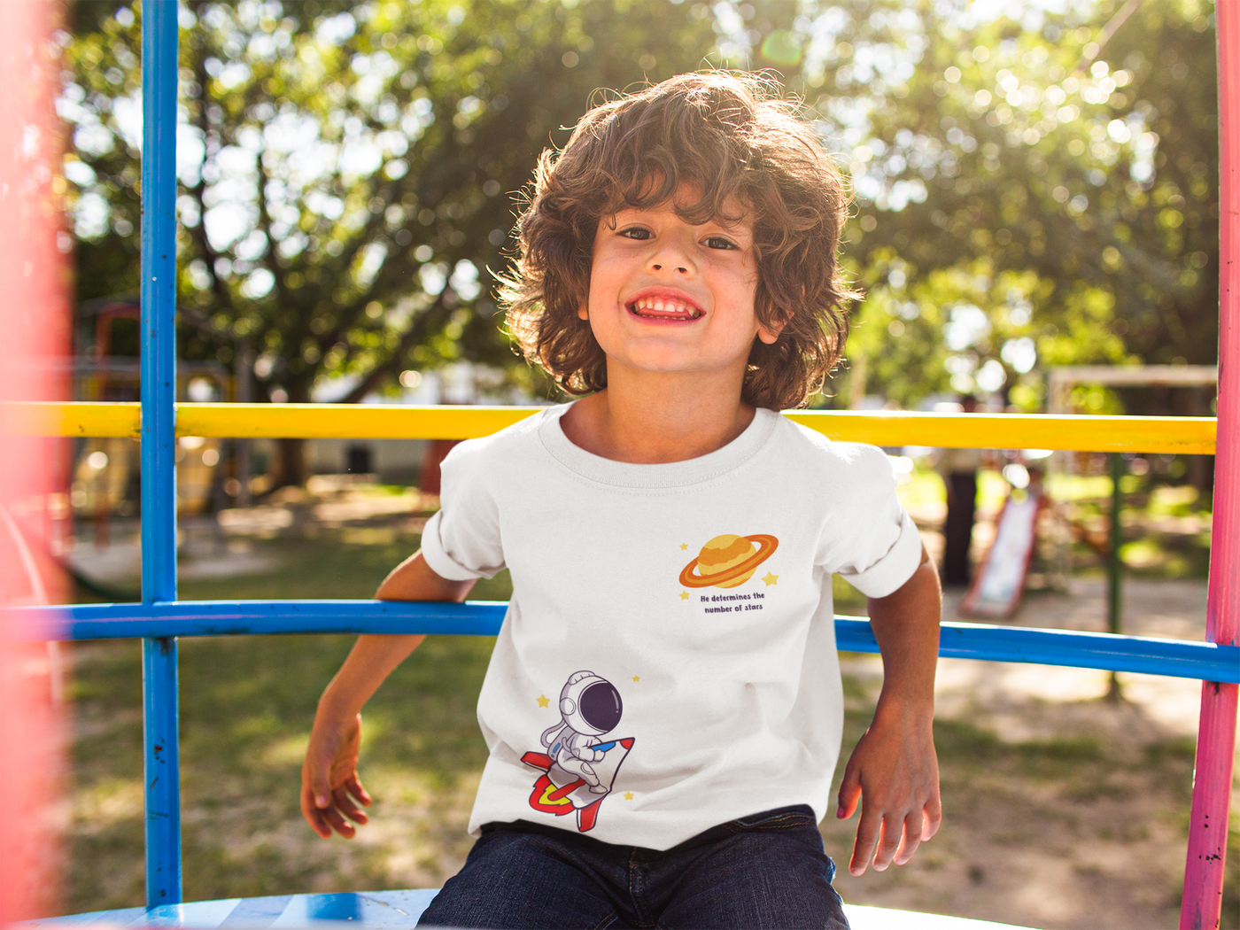 boy sitting on playground with white Christian t-shirt with an outer space theme.